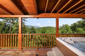 A wooden deck with a hot tub, wooden railings, and a view of a forested landscape.