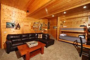 A cozy cabin interior with a leather sofa, a wooden table, and a bunk bed.