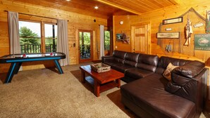 Interior acogedor de una cabaña de madera con mesa de billar, sofá de cuero y una mesa de comedor.