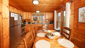 Cocina de cabaña de madera con refrigerador de acero inoxidable, armarios de madera, encimera de granito y una mesa de comedor con individuales.