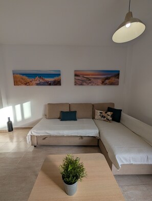 Un salon moderne avec un canapé, une plante en pot et deux œuvres d’art murales sur le thème de la plage.