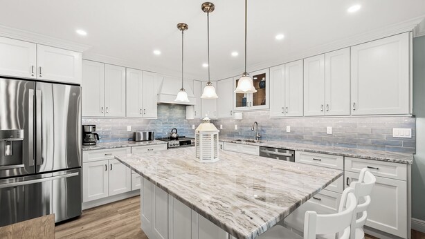 A modern kitchen with white cabinetry, a marble island, stainless steel appliances, and pendant lighting.