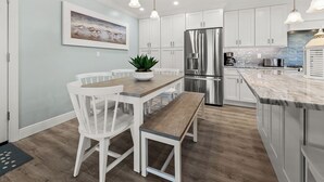 A modern kitchen with white cabinetry, a stainless steel refrigerator, and a marble countertop.
