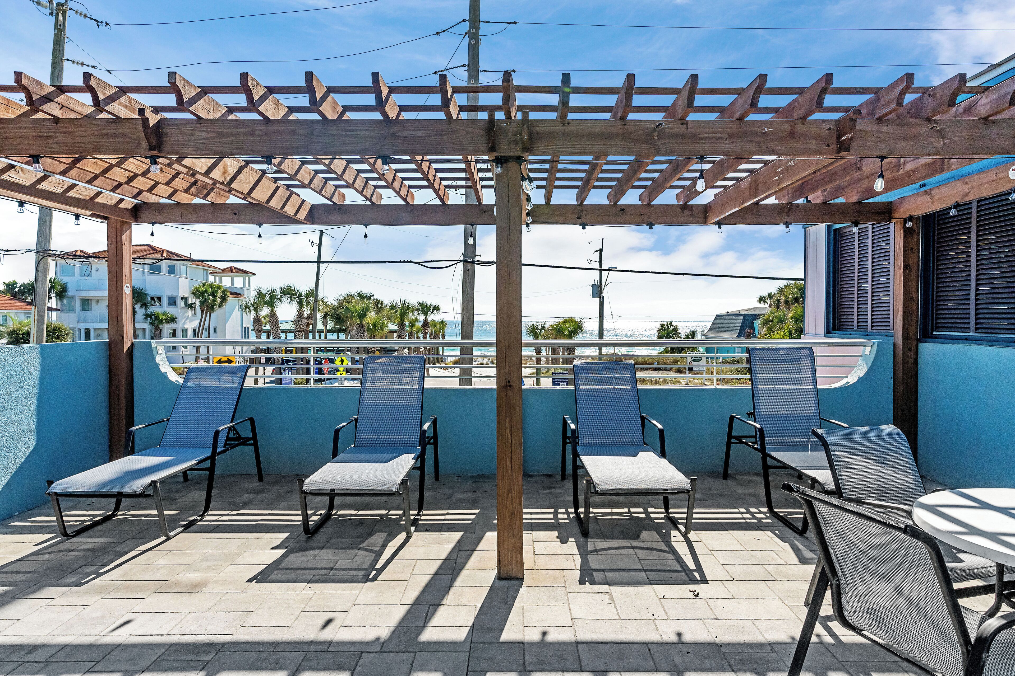 Ein überdachter Außenbereich mit Pergola, mehreren Liegestühlen und Blick auf das Meer.