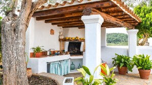 A rustic outdoor kitchen with a stone fireplace, surrounded by potted plants and a pergola. - CASA LAS DALIAS (San Carlos/ Sant Carles de Peralta)