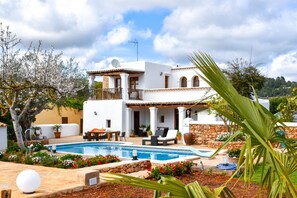 A two-story white villa with a pool, outdoor seating, and a stone wall.