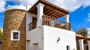 A building with a stone tower, a wooden balcony, and a white facade. - CASA LAS DALIAS (San Carlos/ Sant Carles de Peralta)