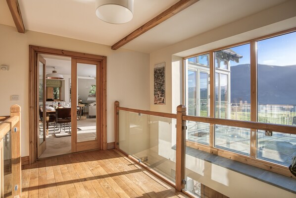 A wooden-floored balcony with glass railings overlooking a mountainous landscape.