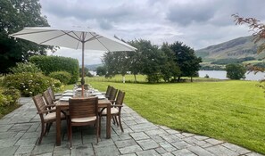 An outdoor dining area with a table set for six, surrounded by chairs, under a large umbrella.