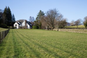 A large, open grassy field with a white house and stone wall in the background.