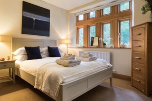 A bedroom with a bed, a nightstand, a dresser, a window with a view of trees, and a painting on the wall.