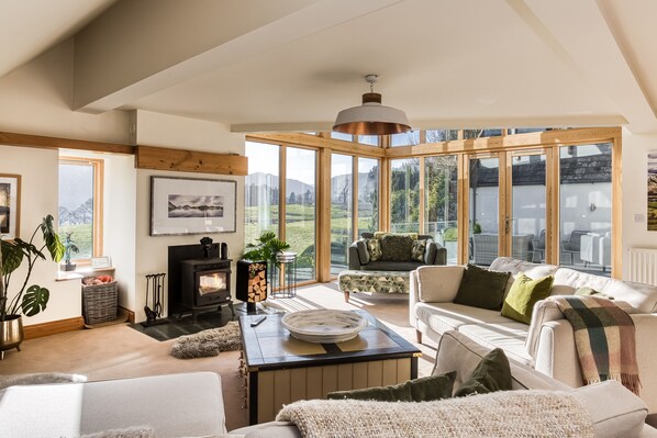 A spacious living room with a fireplace, comfortable seating, and large windows offering a view of the outdoors.