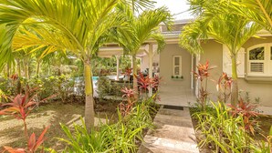 A tropical garden with palm trees and various plants, leading to a building with a tiled entrance. - Areca Palm - luxury villa with private pool, sea and countryside views (Le Vauclin)