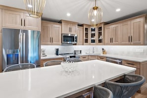 A modern kitchen with wooden cabinets, stainless steel appliances, and a central island with chairs.