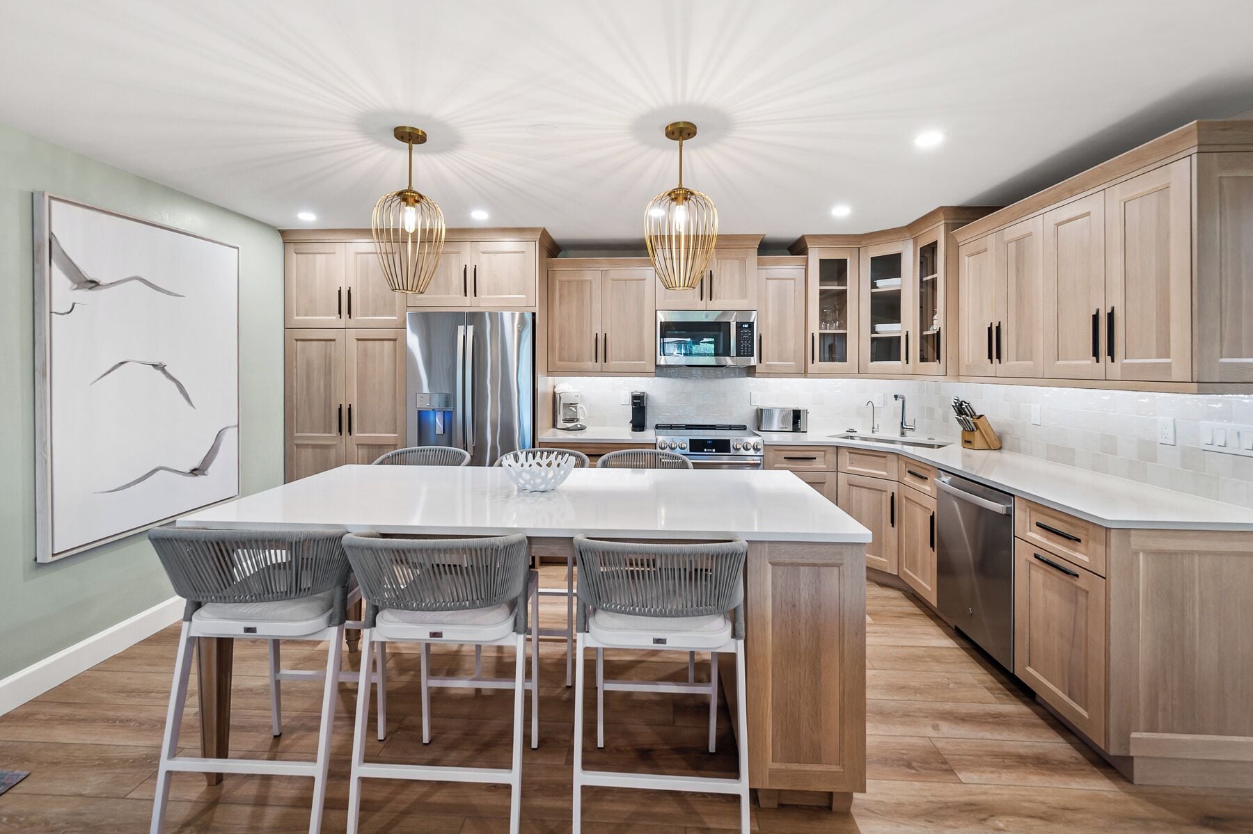 Una cocina moderna con armarios de madera, una isla central con sillas, electrodomésticos de acero inoxidable e iluminación colgante.