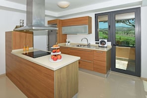 A modern kitchen with a central island, stainless steel appliances, wooden cabinetry, and a view through a glass door. - Salobre Los Lagos 26 (Maspalomas)