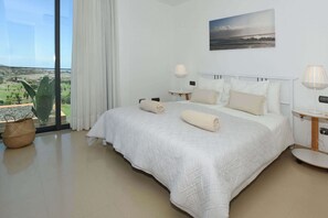 A bedroom with a large bed, two bedside tables, a view of the outdoors, and a painting on the wall. - Salobre Los Lagos 26 (Maspalomas)