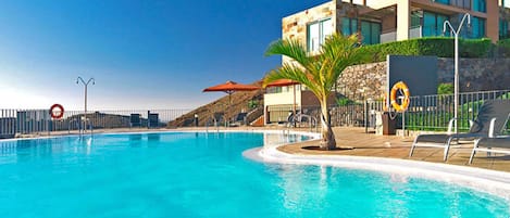 A swimming pool with a lifebuoy, a palm tree, and a modern building in the background.