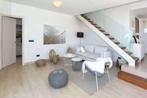 A modern living room with a staircase, a sofa, a coffee table, and decorative items. - Salobre Los Lagos 26 (Maspalomas)