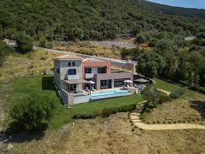 A modern two-story house with a swimming pool, surrounded by a well-maintained lawn and trees.
