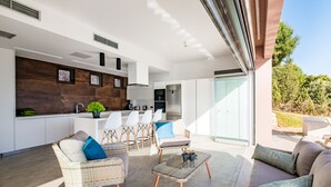 Une cuisine moderne avec des armoires blanches, un mur d’accent en bois et un coin repas doté de meubles en osier.