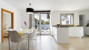 A modern kitchen with a central island, a dining area with a table and chairs, and a view of the outside through large sliding doors.