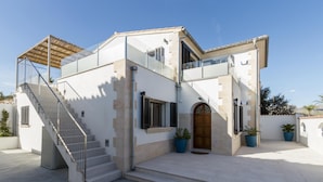 A modern two-story house with a staircase, a wooden door, and potted plants.