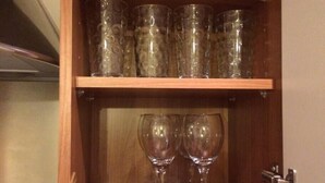Un mobiletto in legno con due bicchieri da vino sullo scaffale inferiore e diversi bicchieri alti sullo scaffale superiore.