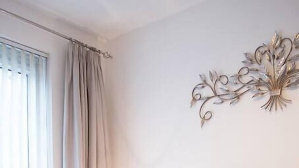 Un letto rifatto con cuscini bianchi e beige, una coperta marrone e asciugamani bianchi arrotolati sul letto.