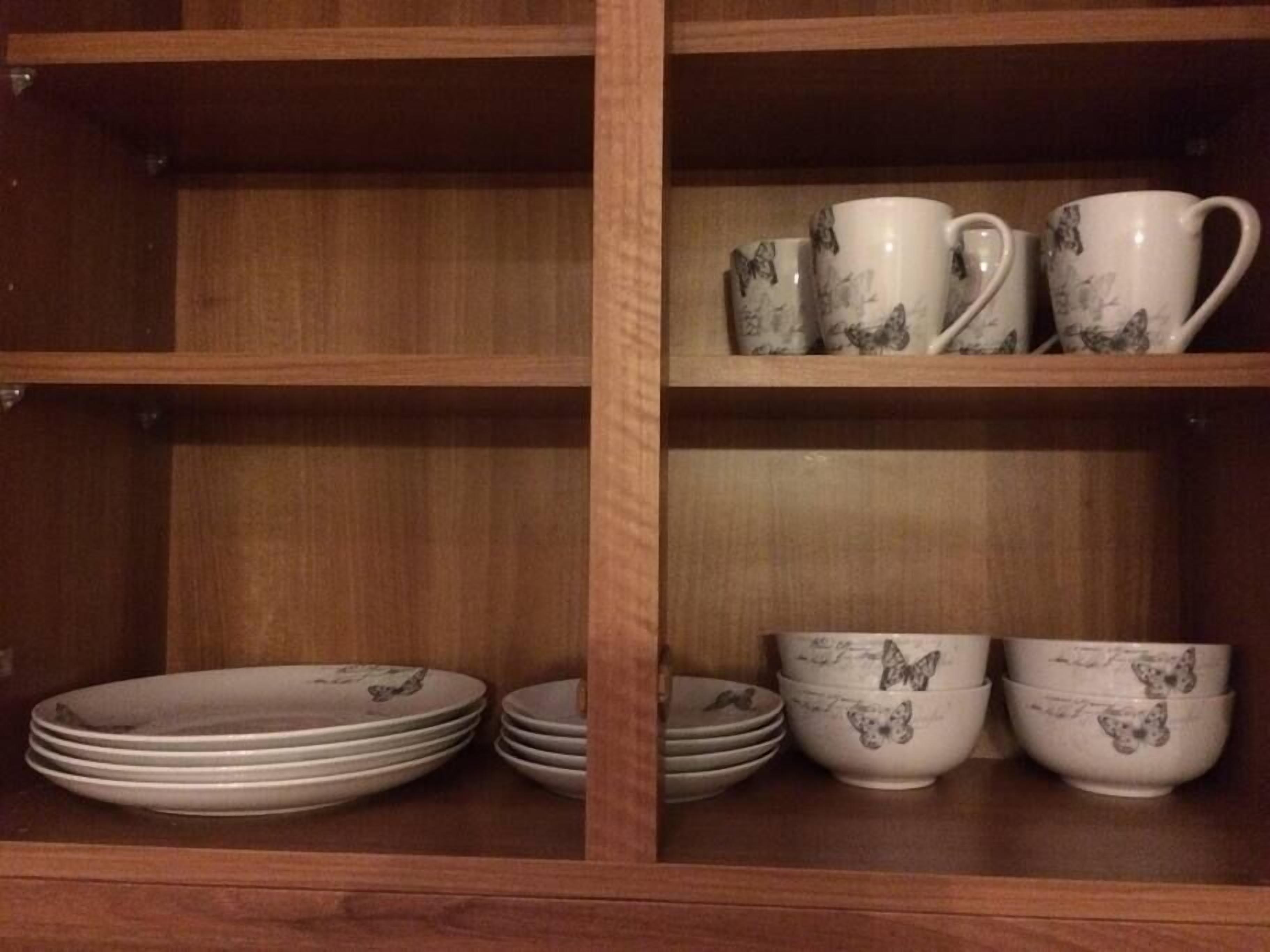 Un mueble de madera con estantes que contiene platos y tazones blancos con diseños de mariposas.