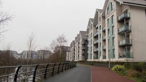 Un edificio moderno con balconi, un vialetto lastricato e un fiume sullo sfondo.
