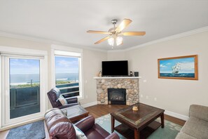 A living room with a fireplace, a television, and a painting. - Promo! Beautiful Oceanfront Condo with Private Hot Tub, Pool, Wifi and More! (Lincoln City)