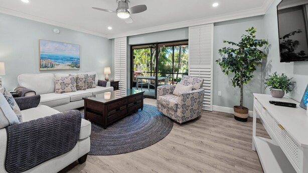 A modern living room with a sofa, armchair, coffee table, and a TV. There is a window with a view of greenery outside. - Newly Renovated Garden View 2 bed, 2 bath at Sanibel Moorings #641 (Sanibel)