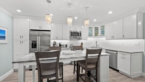 A modern kitchen with white cabinetry, a stainless steel refrigerator, a microwave, and a large island with chairs. - Newly Renovated Garden View 2 bed, 2 bath at Sanibel Moorings #641 (Sanibel)