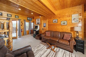 A cozy log cabin interior with a brown leather sofa, a wooden rocking chair, and a small table.