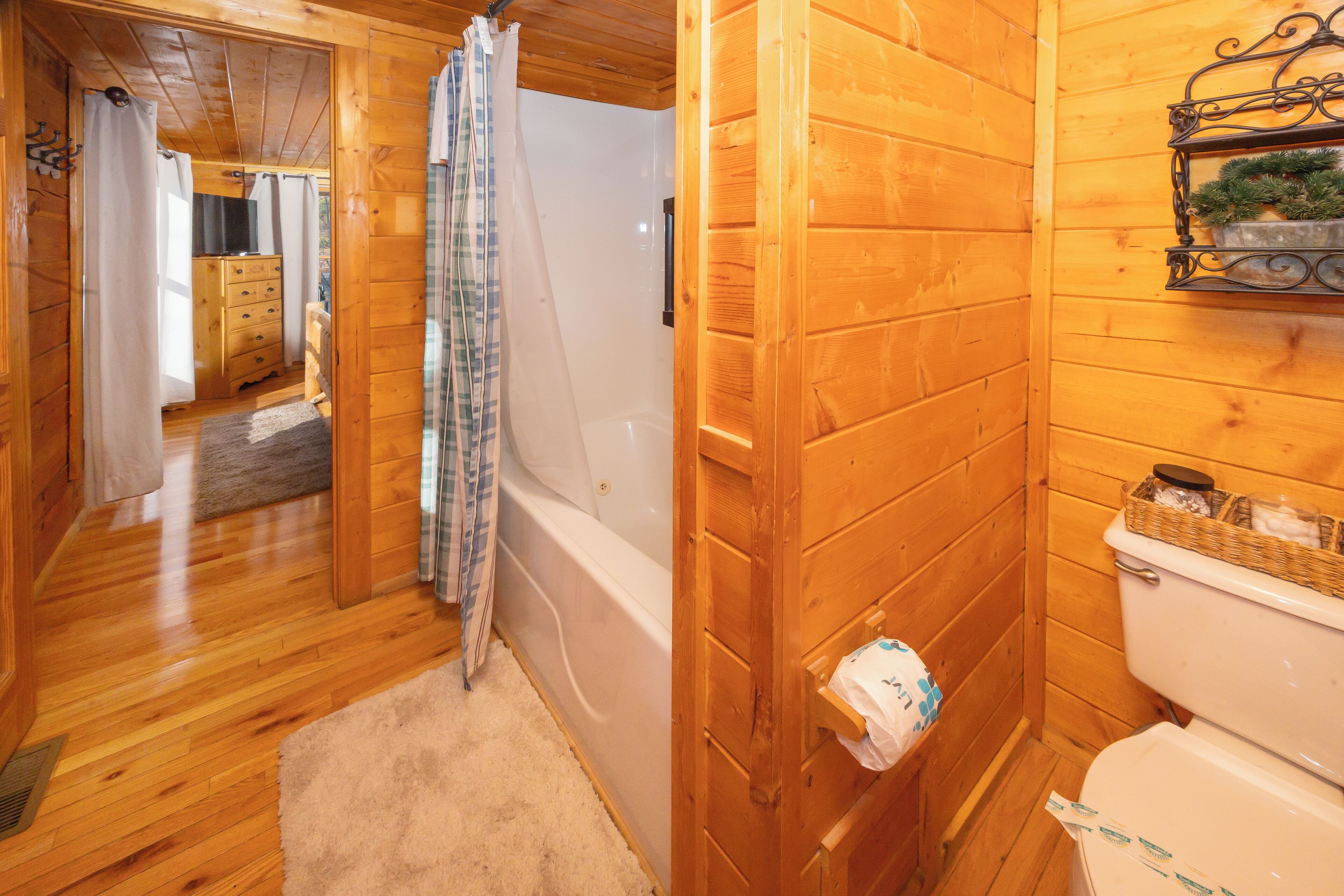 A wooden cabin interior with a wooden floor, a bathtub, a toilet, and a wooden cabinet.