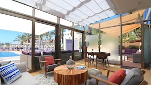 Ein moderner Lounge-Bereich mit Blick auf den Pool, bequeme Sitzgelegenheiten und ein runder Holztisch.