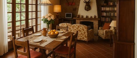 Un comedor con una mesa de madera, sillas, un jarrón con flores y una chimenea decorada con una cabeza de venado.