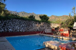 Une piscine avec un mur en pierre, un bordure rouge et une vue sur les montagnes.