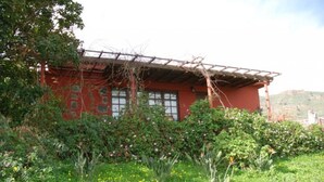 A red building with a wooden pergola, surrounded by lush greenery and flowering plants.