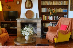Una sala de estar con chimenea, una estantería, un televisor y un sillón amarillo.