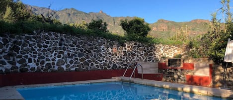 Piscina com muro de pedra, borda vermelha e vista para montanhas.