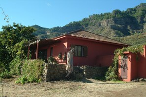 Un bâtiment rouge avec un mur en pierre, une structure en bois sur la gauche et un paysage montagneux en arrière-plan.