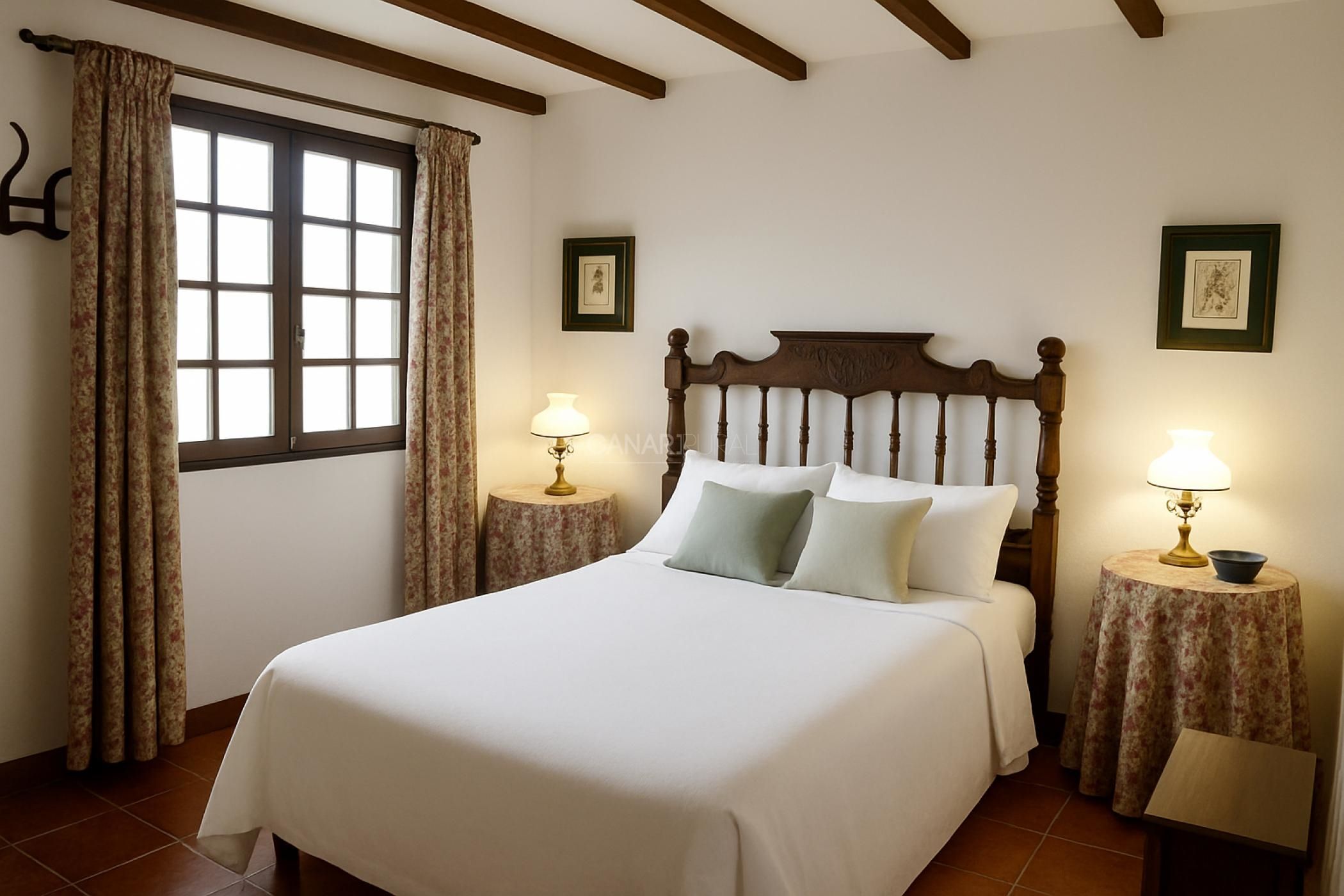 Une chambre avec un grand lit, deux tables de chevet avec des lampes, une fenêtre avec des rideaux et des poutres en bois au plafond.