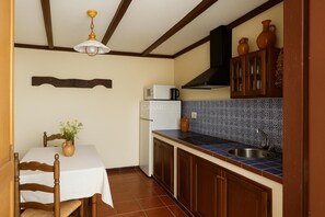Une cuisine avec une table blanche, des chaises en bois, un four à micro-ondes, un évier et un mur recouvert de carreaux.