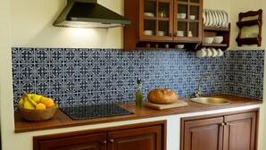 A kitchen with blue and white patterned tiles, wooden cabinets, a bread loaf, a fruit basket, and a sink.