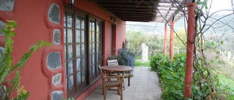 A covered patio with a table and chairs, stone wall, and potted plants.