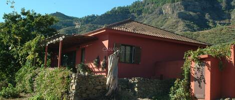 Un edificio rojo con un muro de piedra, una estructura de madera a la izquierda y montañas al fondo.