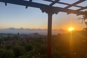 A sunset view from a covered outdoor area with a pergola structure.