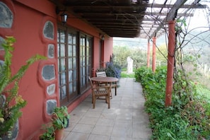 Eine überdachte Terrasse mit Tisch, Stühlen, einer Steinmauer und Topfpflanzen.